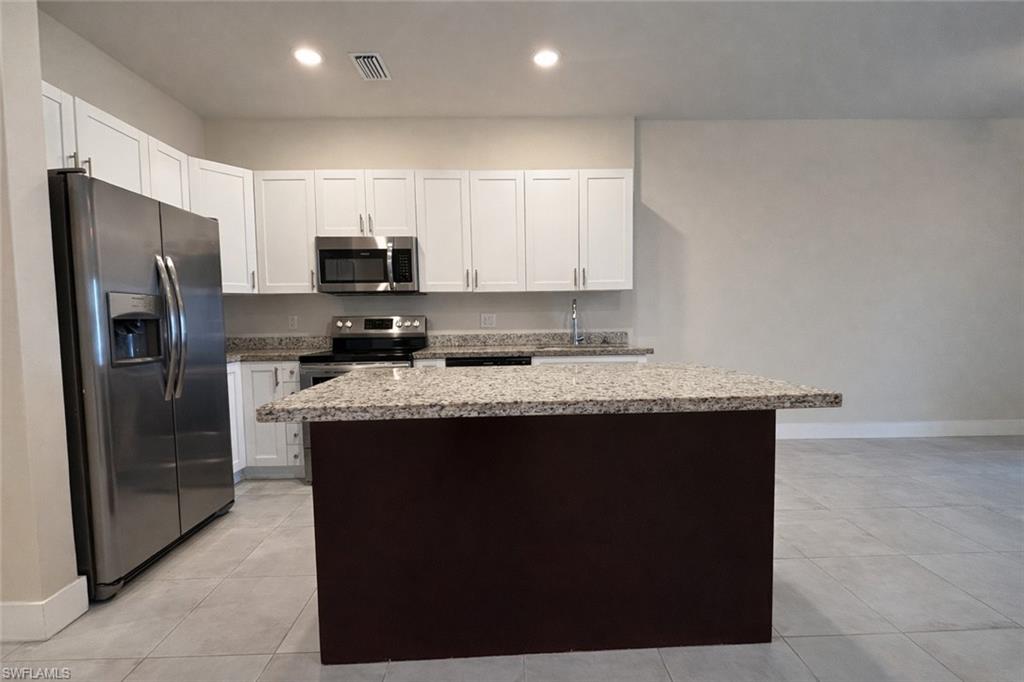 Kitchen featuring white cabinetry, a center island, a ceiling fan, open floor plan, and stainless steel appliances