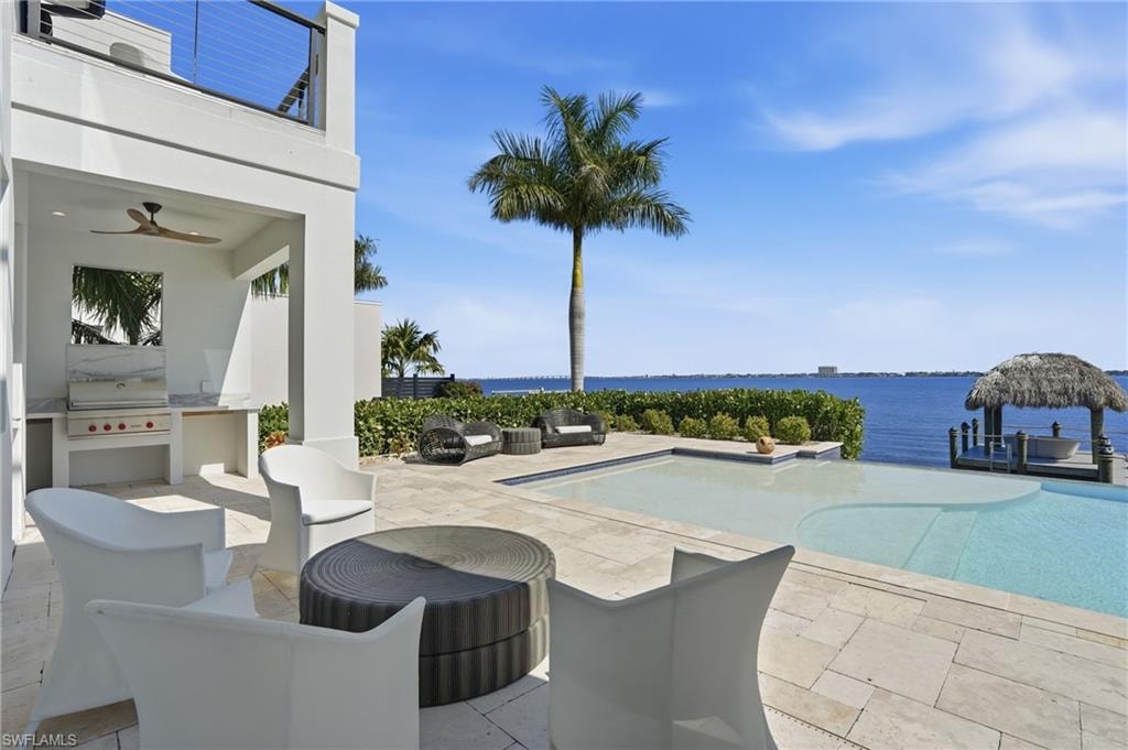 Swimming pool with a patio area, an outdoor kitchen with living area, and a water view