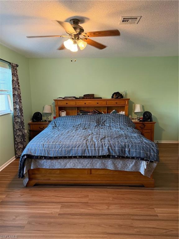 Bedroom with a textured ceiling, wood finished floors, and a ceiling fan
