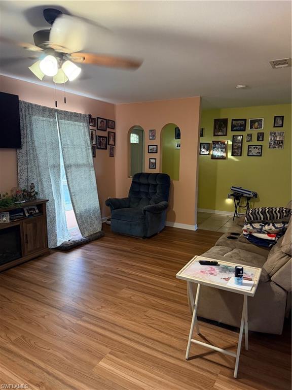 Living room with a ceiling fan, arched walkways, and light wood finished floors