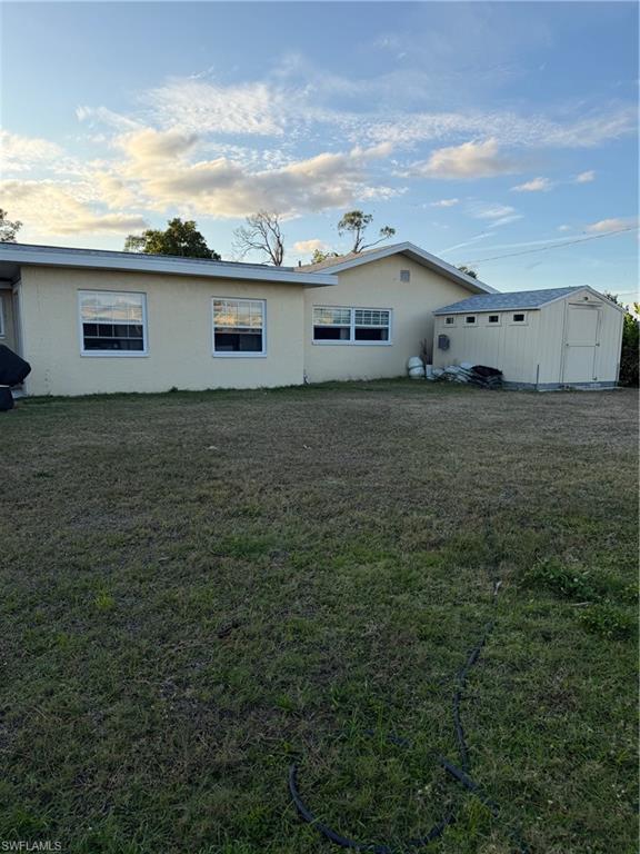 Rear view of house with a storage unit, stucco siding, and a lawn