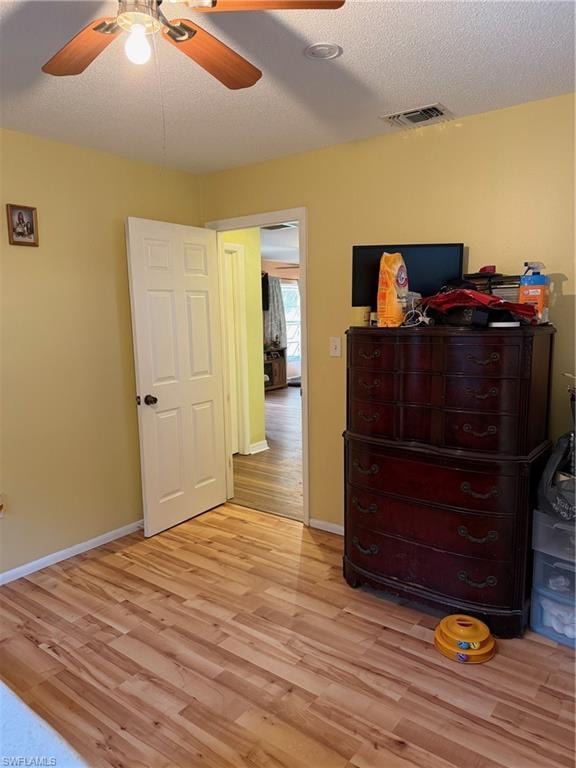 Bedroom with light wood finished floors, ceiling fan, and a textured ceiling