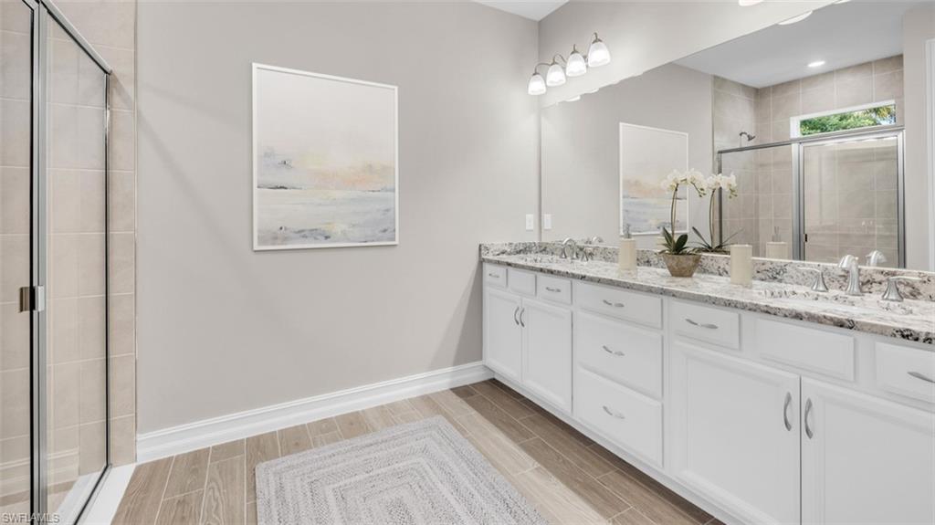 This image is virtually staged. Bathroom featuring a stall shower, double vanity, and wood tiled floors
