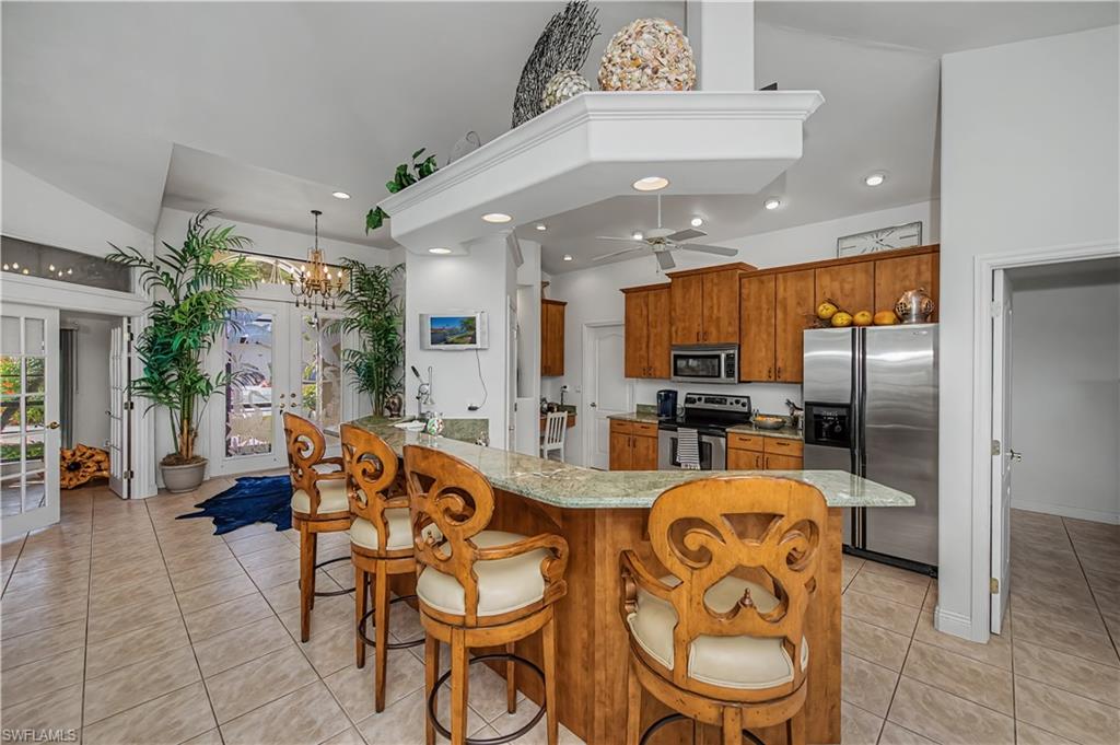 Kitchen featuring wood finish cabinets, stainless steel appliances, light stone countertops, a kitchen breakfast bar, and suspended lighting