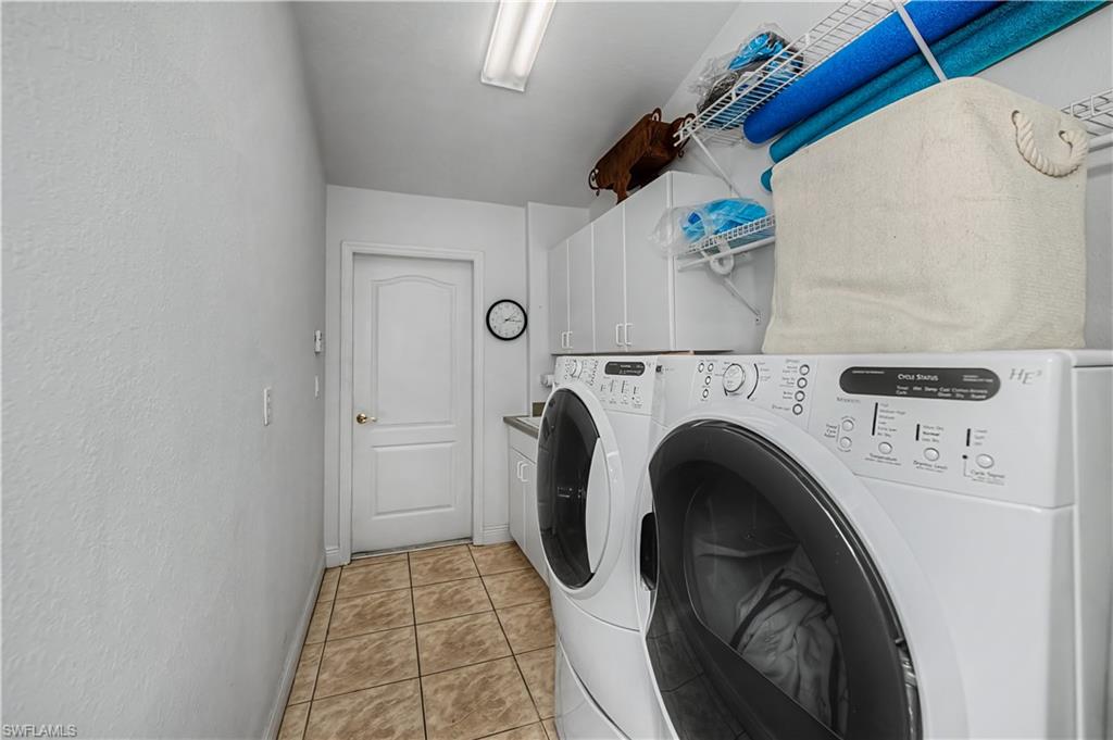 Laundry area with washing machine and clothes dryer, cabinet space, light tile patterned flooring, and a textured wall