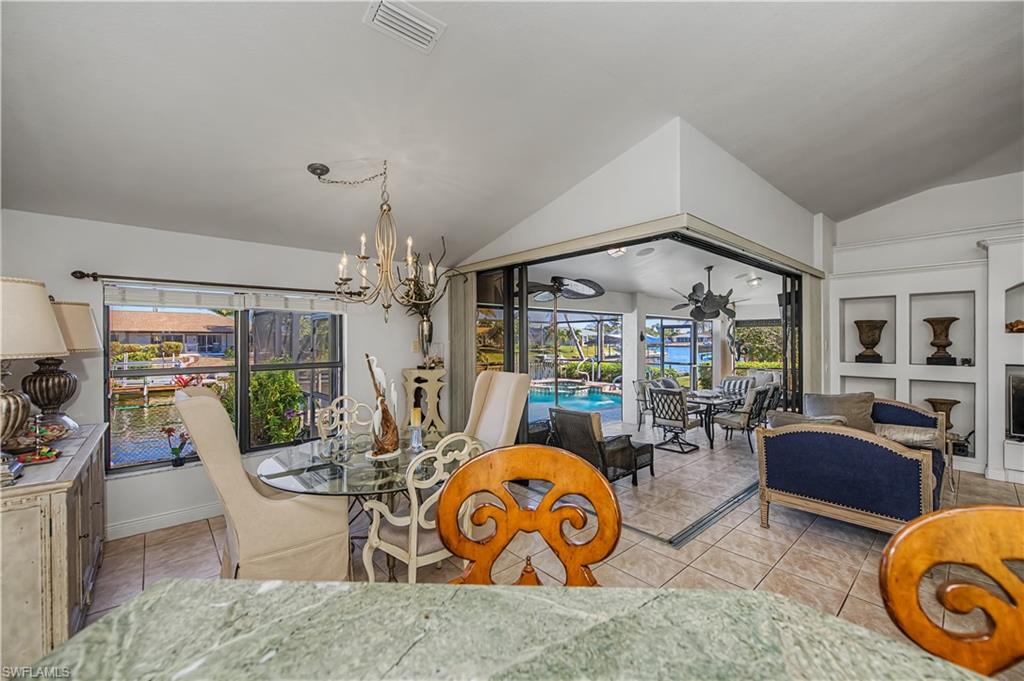 Tiled dining room with a chandelier, a sunroom, vaulted ceiling, a fireplace, and a ceiling fan
