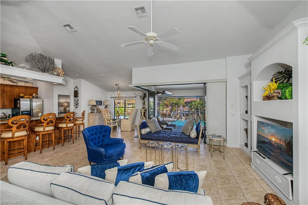 Living area with a ceiling fan, hanging lights, vaulted ceiling, built in shelves, and light tile patterned floors