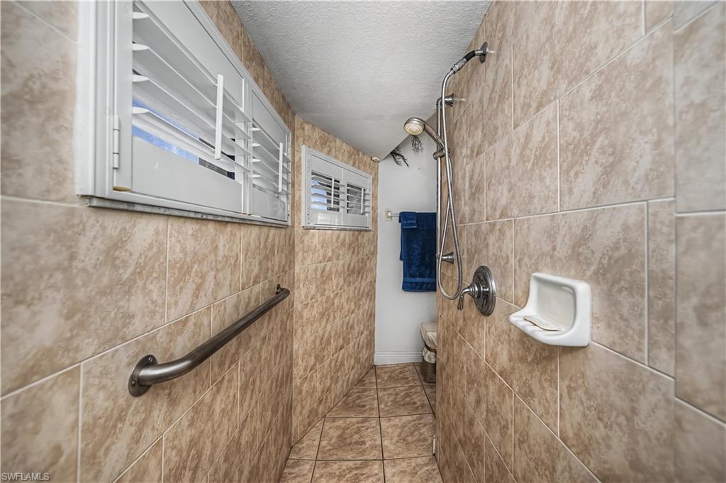 Full bathroom featuring a textured ceiling, a tile shower, and tile walls