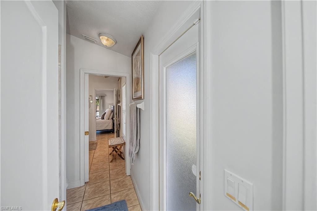 Hallway featuring vaulted ceiling and light tile patterned floors