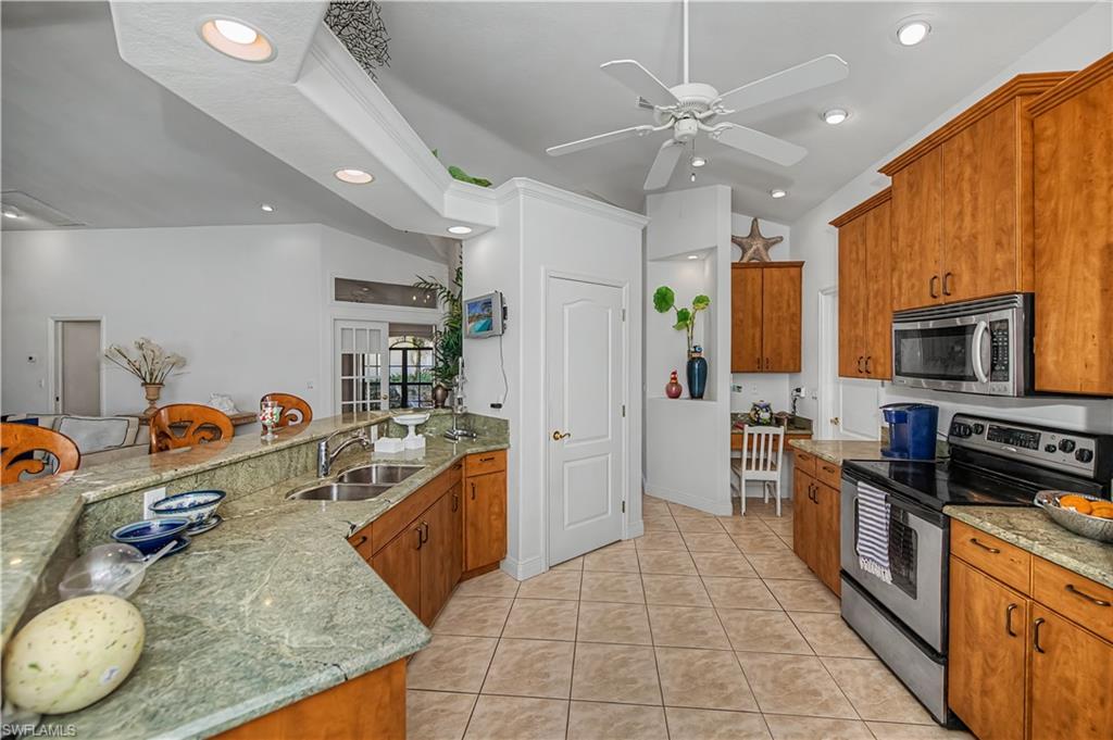 Kitchen featuring stainless steel appliances, wood finish cabinets, light stone countertops, a peninsula, and a ceiling fan