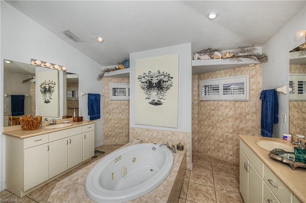 Full bathroom featuring two vanities, vaulted ceiling, a whirlpool tub, and light tile patterned flooring