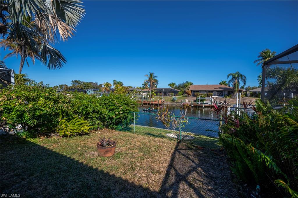 View of green lawn featuring a water view, a boat dock, a lanai, and boat lift