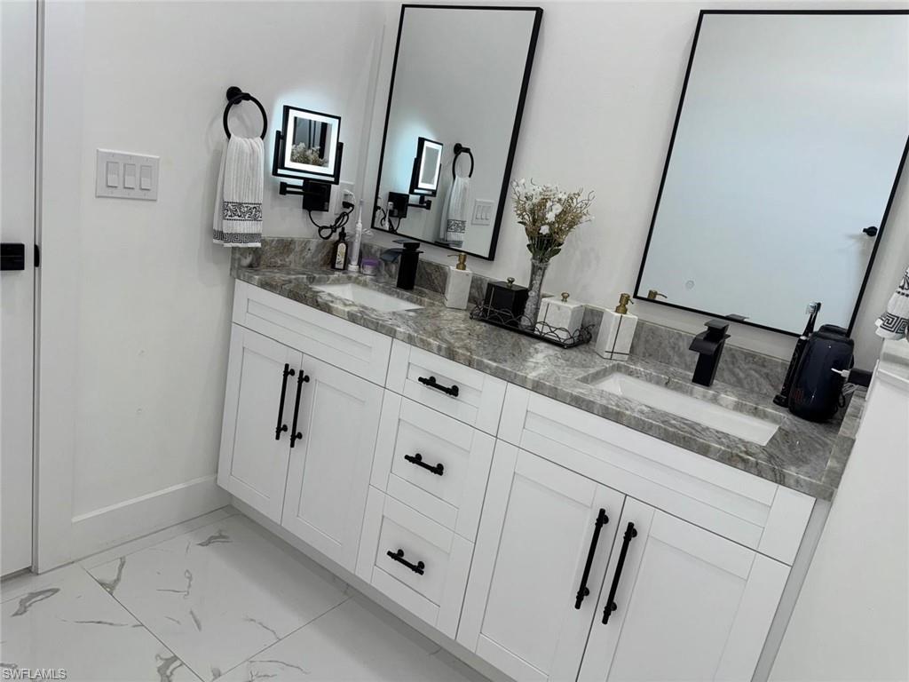 Full bathroom featuring double vanity, marble finish floor, baseboards, and a sink