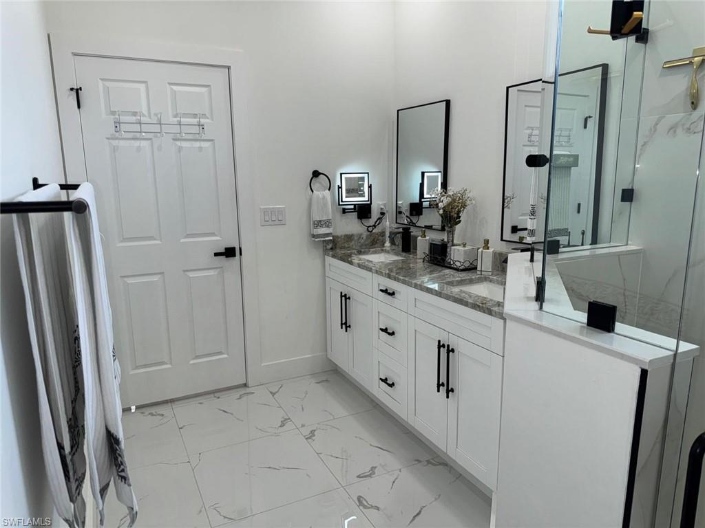 Bathroom featuring double vanity, marble finish floor, a stall shower, and a sink
