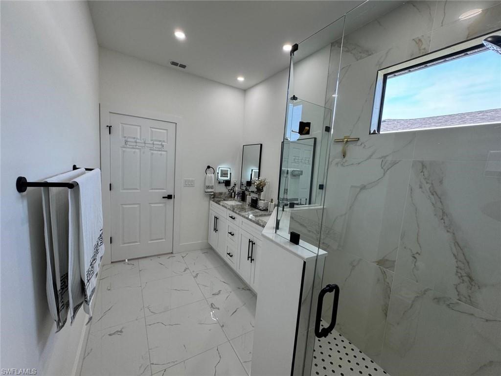 Full bathroom featuring a marble finish shower, visible vents, marble finish floor, and double vanity