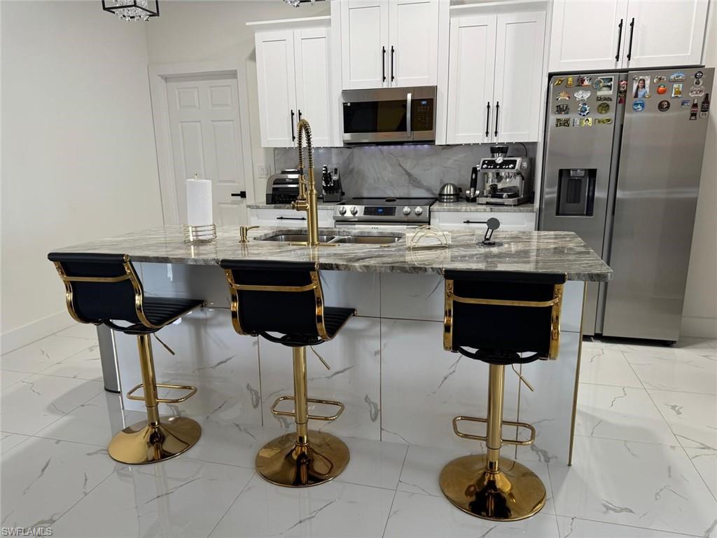 Kitchen featuring marble finish floor, a sink, stainless steel appliances, decorative backsplash, and light stone countertops
