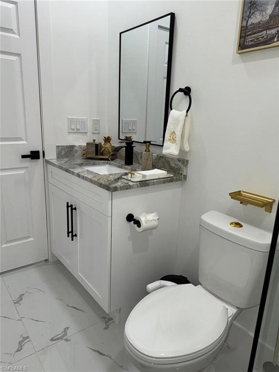 Half bath with vanity, toilet, and marble finish floor