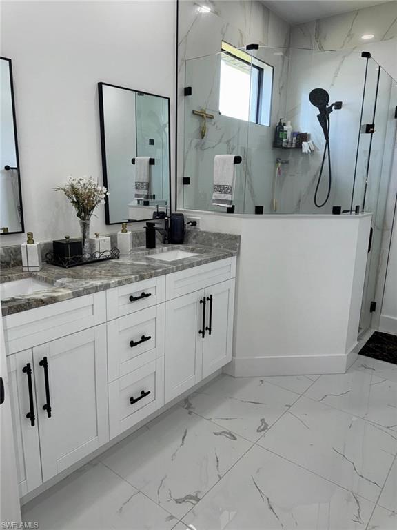 Bathroom with double vanity, marble finish floor, a marble finish shower, and a sink