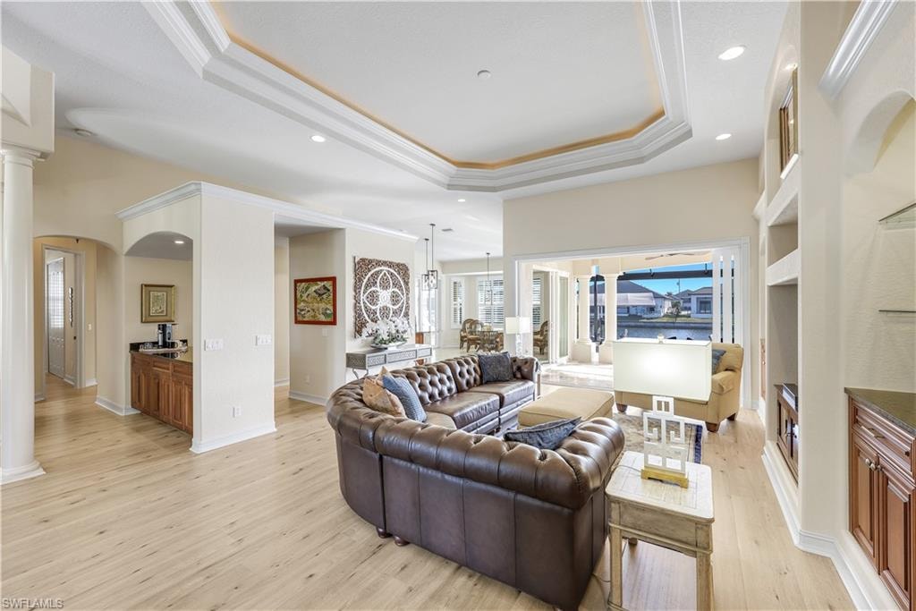 Living area featuring ornamental molding, decorative columns, recessed lighting, light wood-style floors, and a tray ceiling