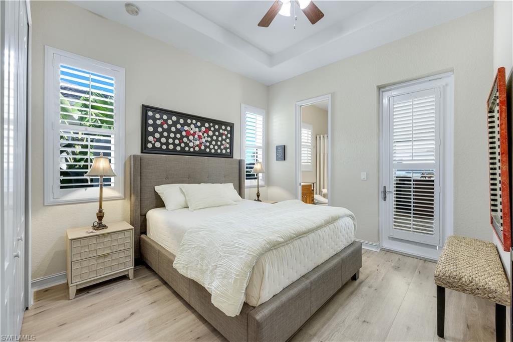 Bedroom with light wood finished floors, ceiling fan, multiple windows, and a raised ceiling