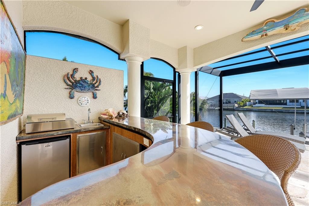 View of patio with exterior kitchen, a water view, glass enclosure, and a dock