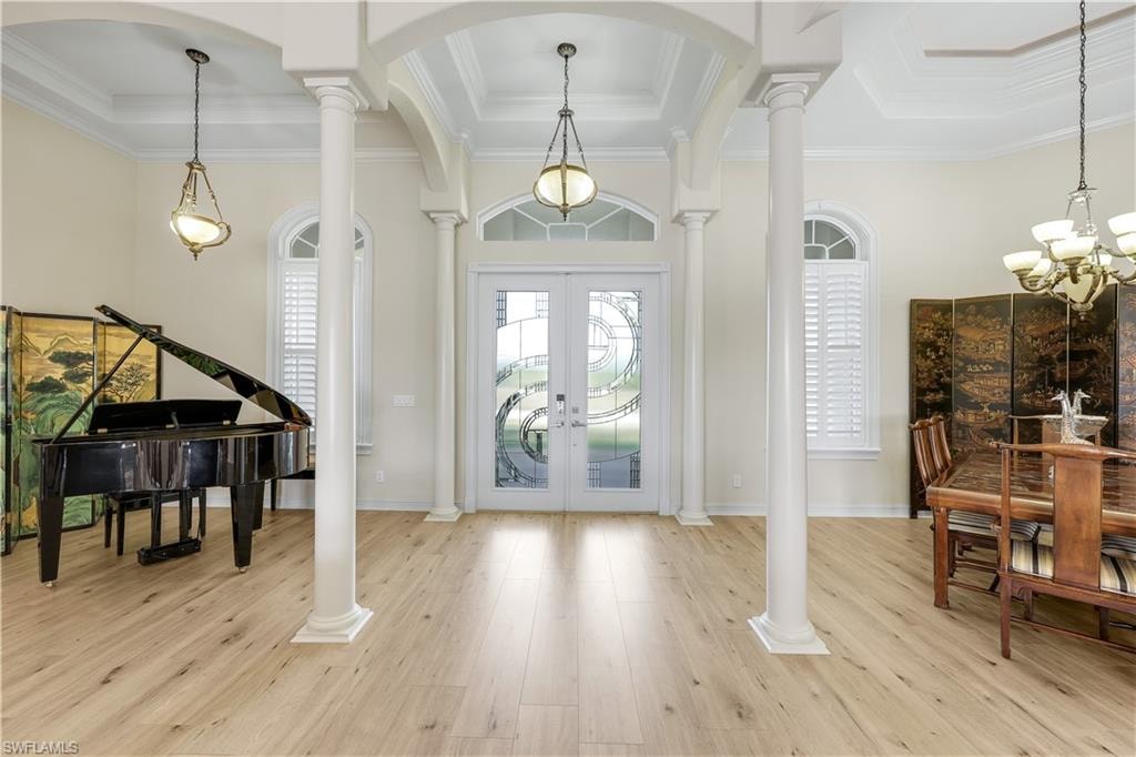 Entrance foyer featuring decorative columns, french doors, a chandelier, light wood-style flooring, and arched walkways