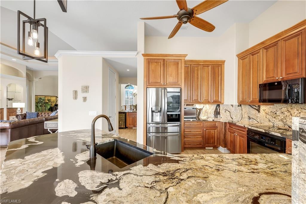 Kitchen with a ceiling fan, light stone counters, black appliances, wood finish cabinetry, and arched walkways