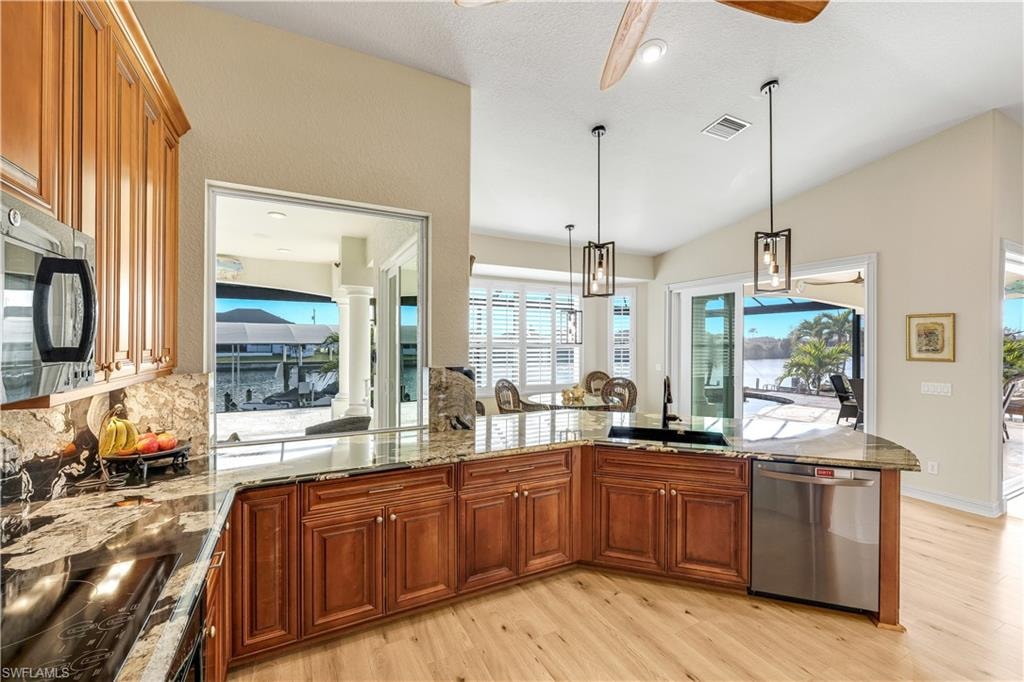 Kitchen featuring a peninsula, light stone countertops, stainless steel appliances, light wood-style floors, and decorative light fixtures
