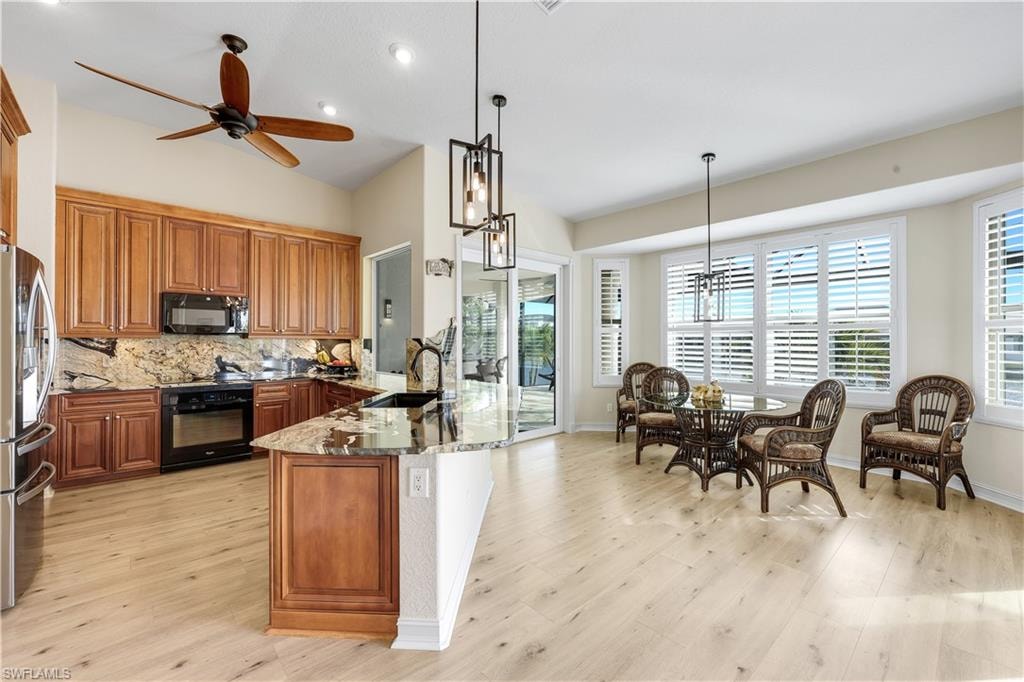 Kitchen with wood finish cabinetry, light stone counters, black appliances, a chandelier, and backsplash