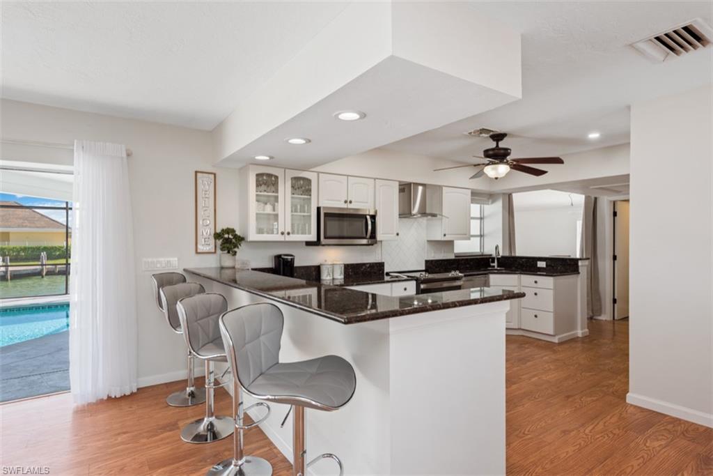 Kitchen with a peninsula, white cabinetry, a kitchen breakfast bar, dark stone countertops, and recessed lighting