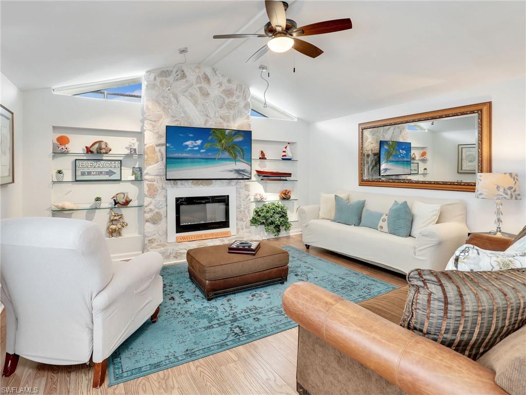 Living room featuring built in features, a stone fireplace, ceiling fan, wood finished floors, and beamed ceiling