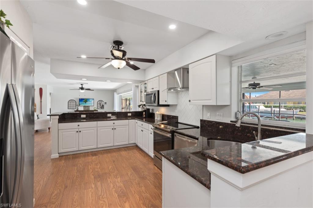 Kitchen with ceiling fan, a peninsula, backsplash, dark stone countertops, and stainless steel appliances