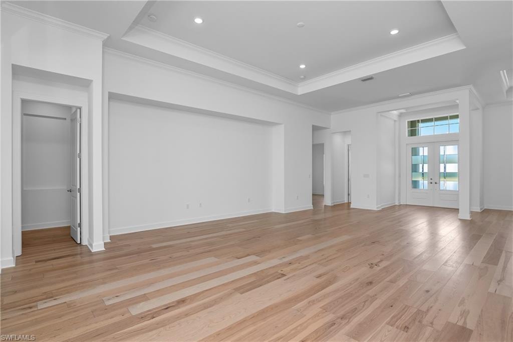 Unfurnished living room with french doors, light wood-style flooring, a raised ceiling, crown molding, and recessed lighting
