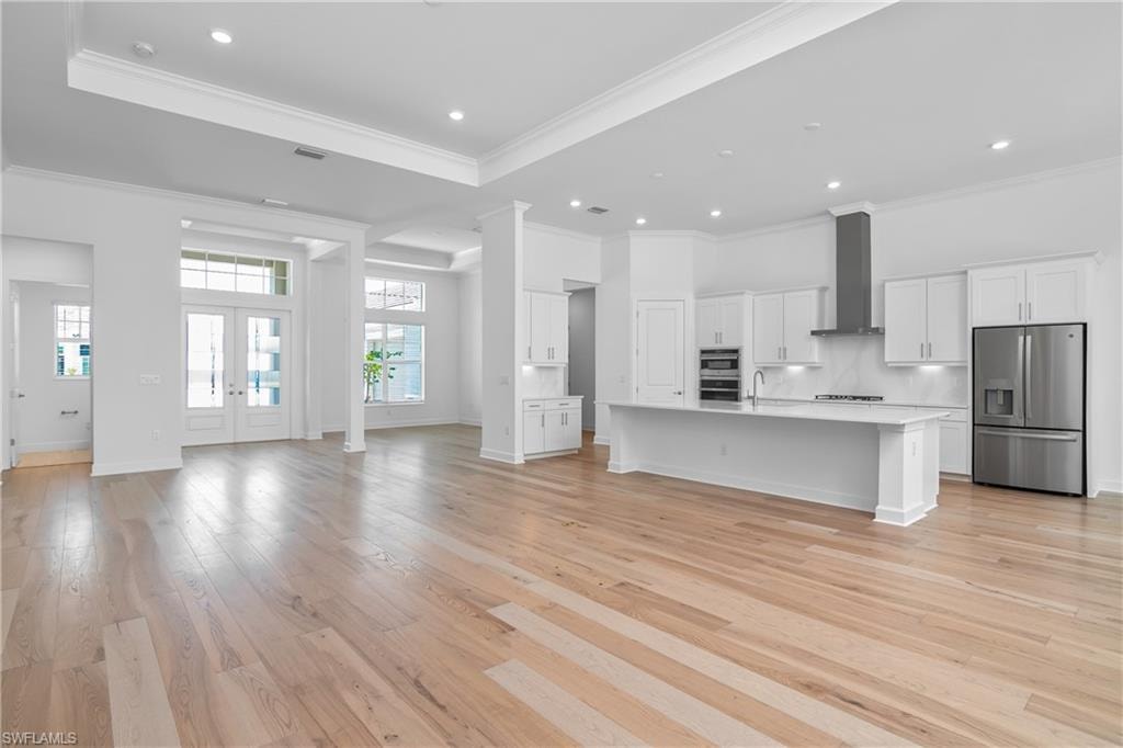Kitchen featuring open floor plan, an island with sink, stainless steel appliances, white cabinetry, and french doors