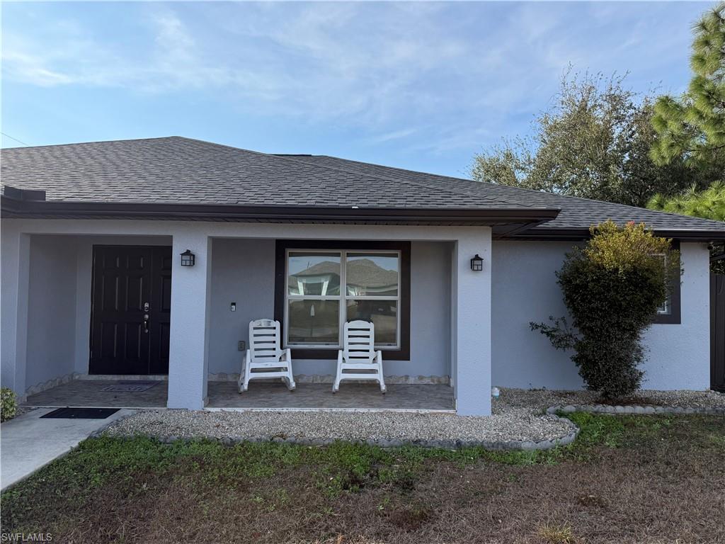 Entrance to property featuring a shingled roof, stucco siding, and a porch