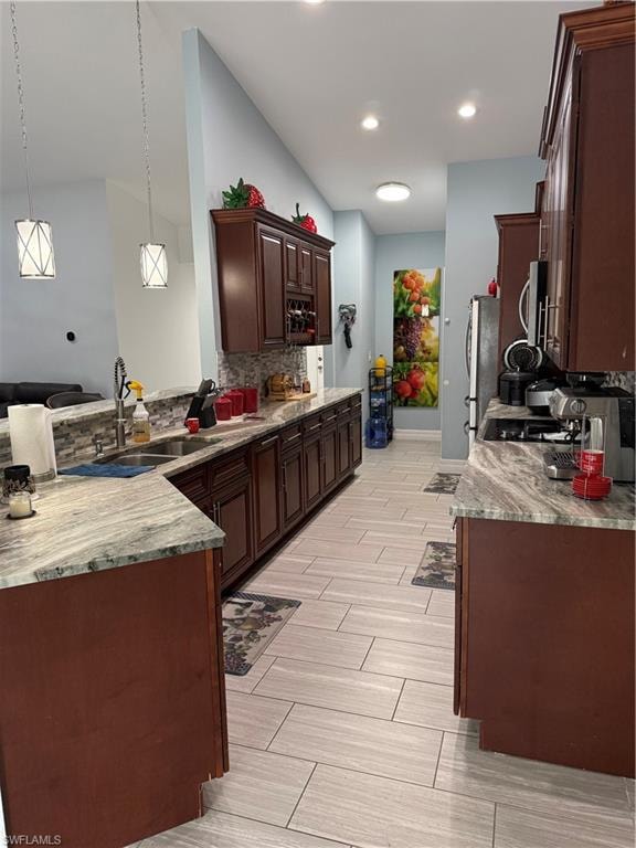 Kitchen with a peninsula, light stone counters, hanging light fixtures, dark wood finish cabinetry, and tasteful backsplash