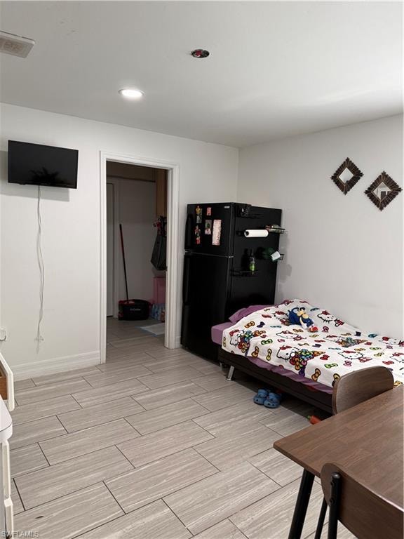 Bedroom with freestanding refrigerator, wood finish floors, and a spacious closet