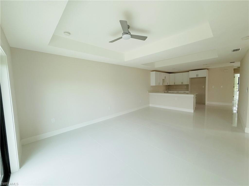 Unfurnished living room featuring a tray ceiling, ceiling fan, and light tile patterned flooring