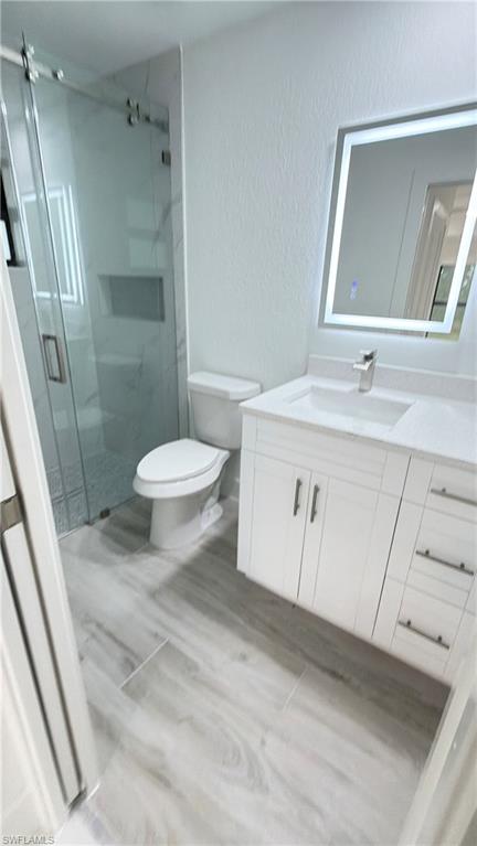 Bathroom with vanity, a textured wall, a marble finish shower, and light wood-style floors