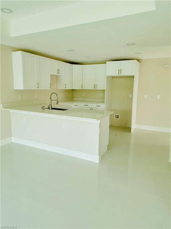 Kitchen featuring white cabinets, a peninsula, light tile patterned flooring, and light stone countertops