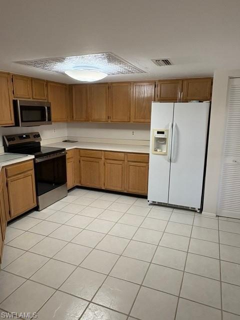 Kitchen with stainless steel appliances, light countertops, light tile patterned floors, and wood finish cabinetry