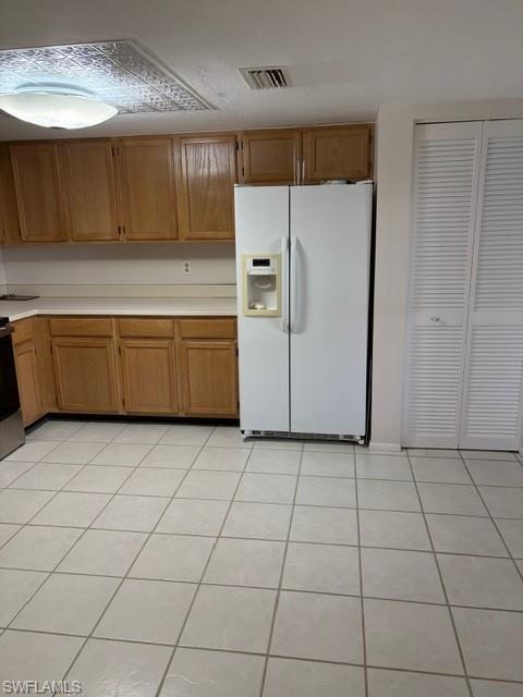 Kitchen featuring white refrigerator with ice dispenser, light tile patterned flooring, light countertops, stainless steel stove, and wood finish cabinets