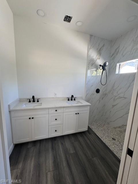 Bathroom with double vanity, a marble finish shower, and dark wood finished floors