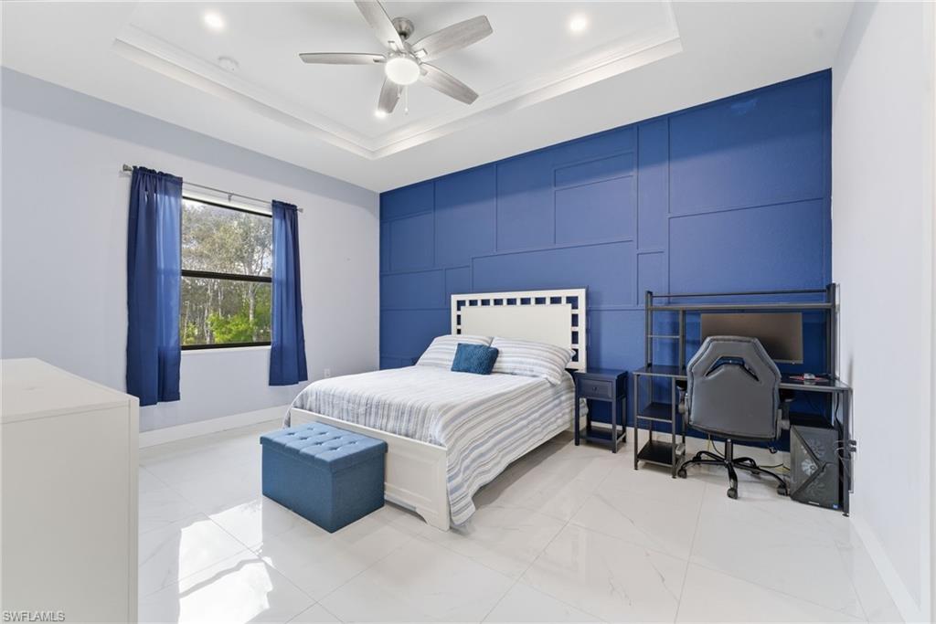 Bedroom featuring a ceiling fan, a tray ceiling, a desk, and an accent wall