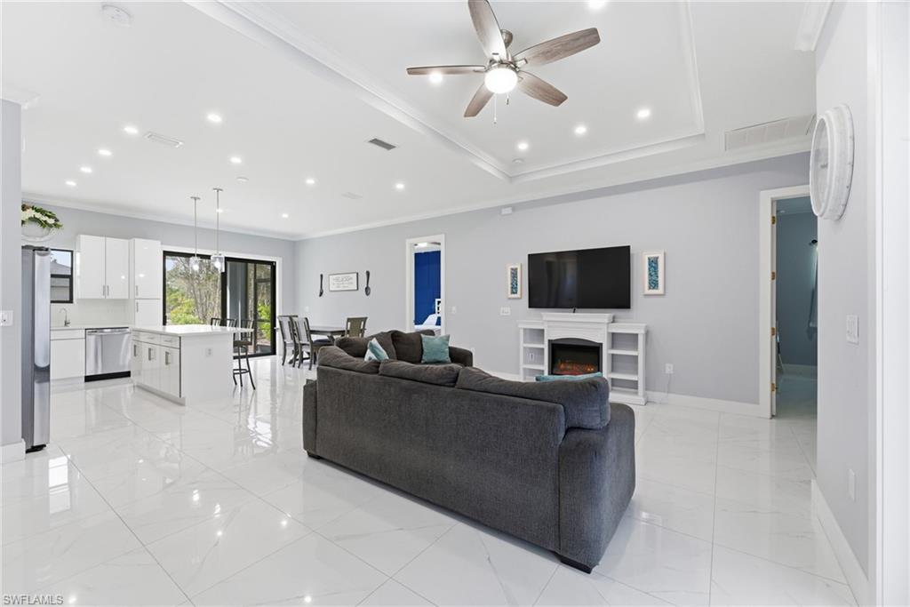 Living area with crown molding, a ceiling fan, recessed lighting, and a warm lit fireplace