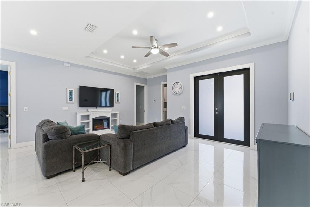 Living room featuring french doors, crown molding, ceiling fan, a warm lit fireplace, and a tray ceiling