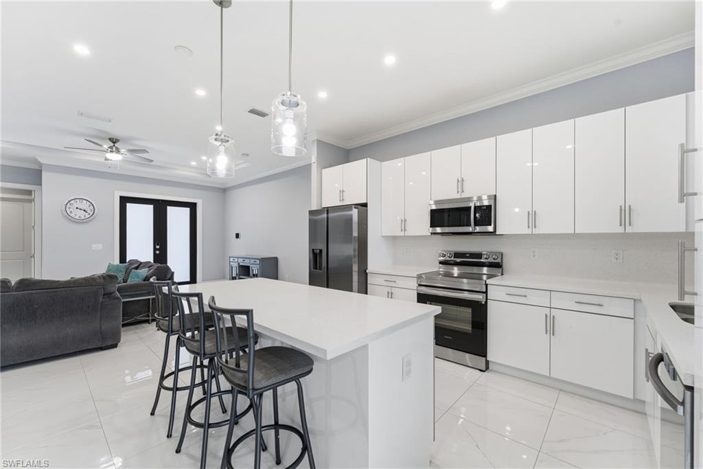 Kitchen featuring hanging light fixtures, stainless steel appliances, a center island, a breakfast bar, and white cabinetry