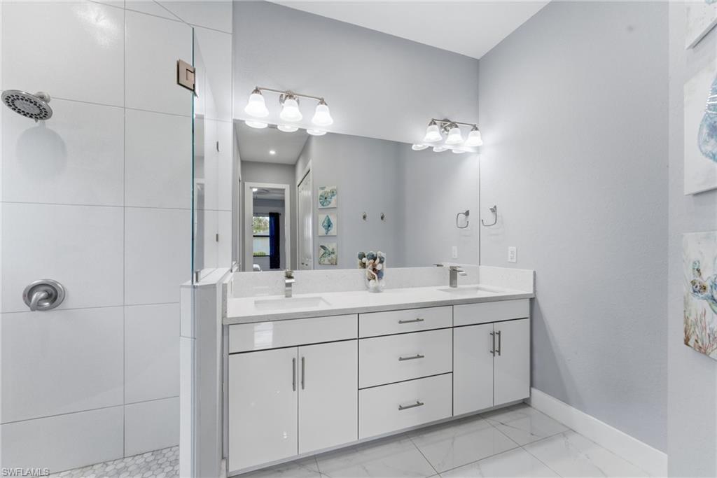 Full bathroom featuring double vanity, a tile shower, and light marble finish floors
