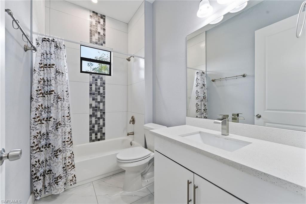Bathroom with vanity, shower / tub combo, and light marble finish flooring