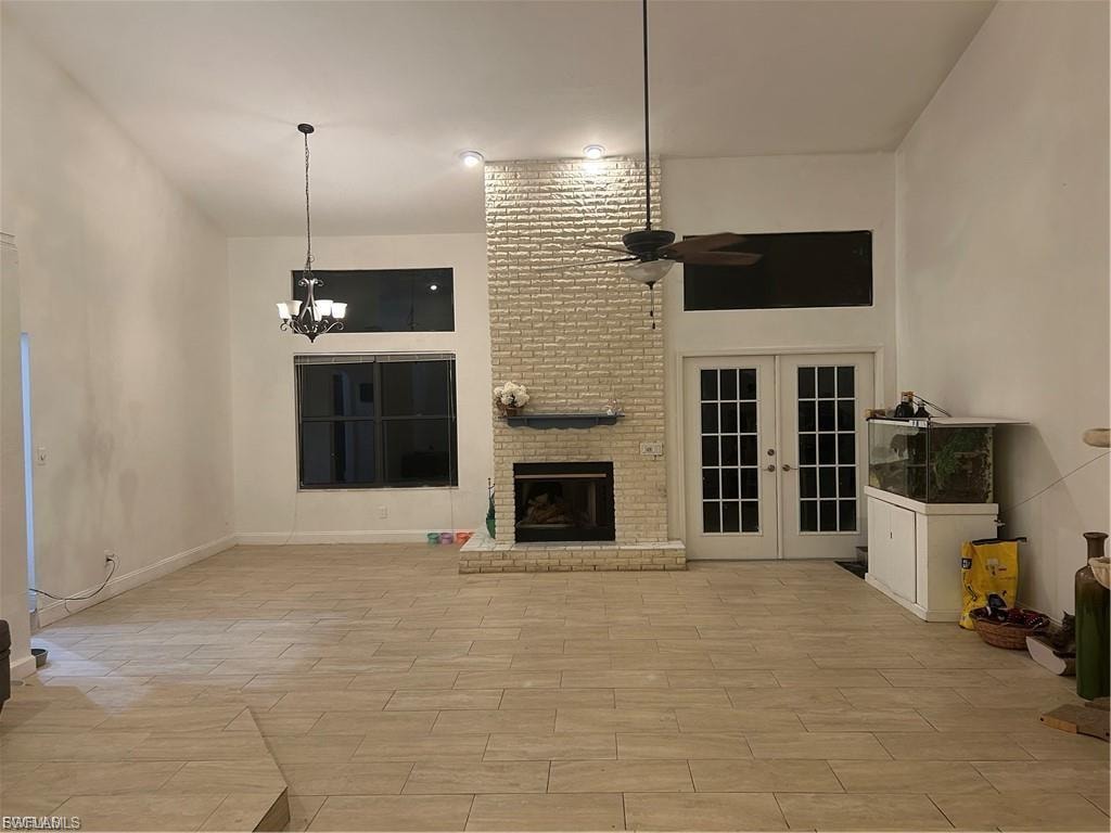 Unfurnished living room featuring french doors, a ceiling fan, hanging lights, a brick fireplace, and wood finish floors